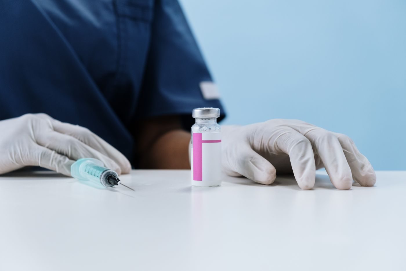 Mãos com luvas ao lado de uma seringa e um frasco de medicamento